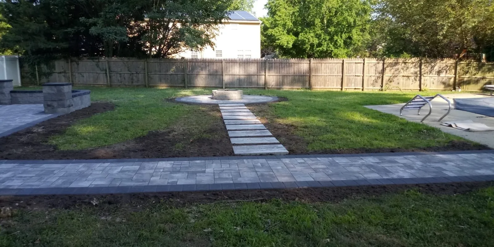 Gray paver walkway connecting a backyard patio, pool, and round fire pit, built by New Jersey Pavers