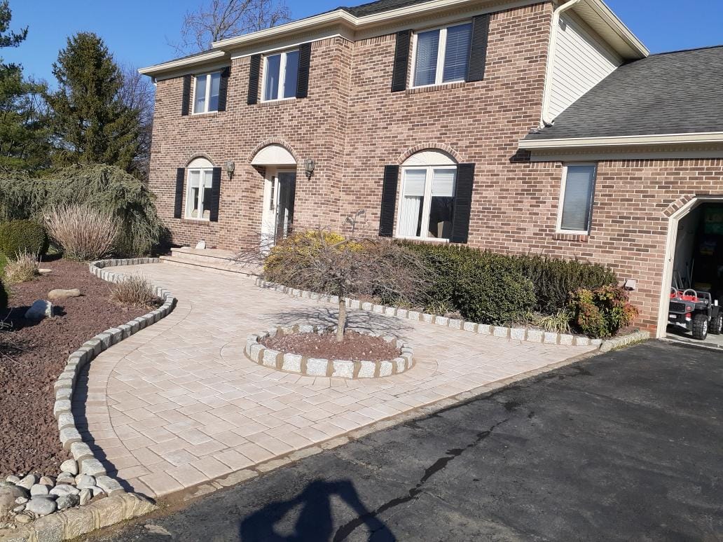 Curved tan paver walkway with a circular tree bed and stone edging, built by New Jersey Pavers