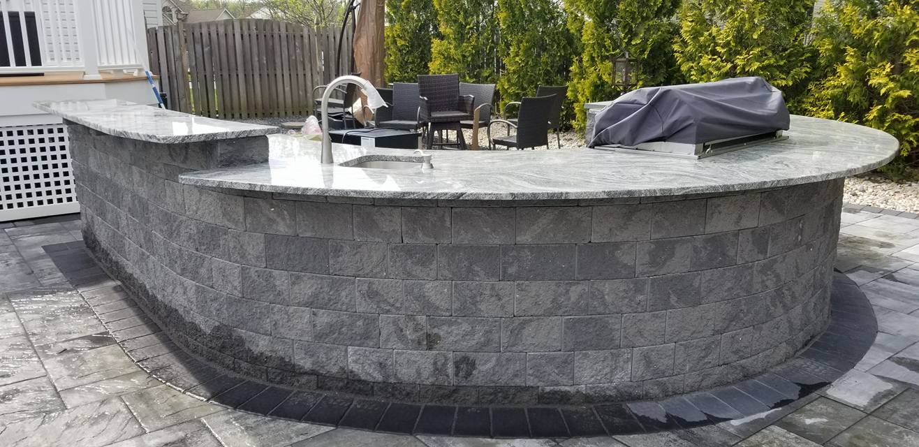 Curved stone outdoor kitchen island with granite counter and grill
