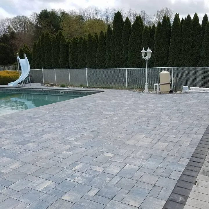 Large gray paver pool deck with a dark border beside a backyard pool