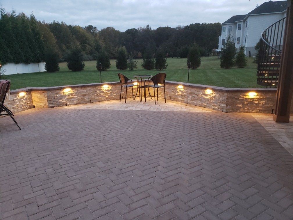 Herringbone paver patio with a lighted stone wall