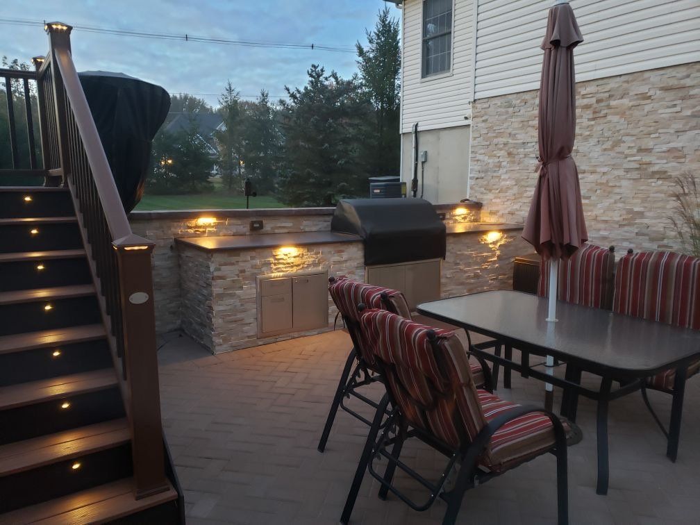 Outdoor dining patio with a grill island and illuminated steps in Freehold, New Jersey, by New Jersey Pavers