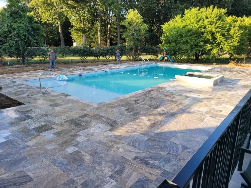 Travertine pool deck surrounding a rectangular pool and raised spa, built by New Jersey Pavers