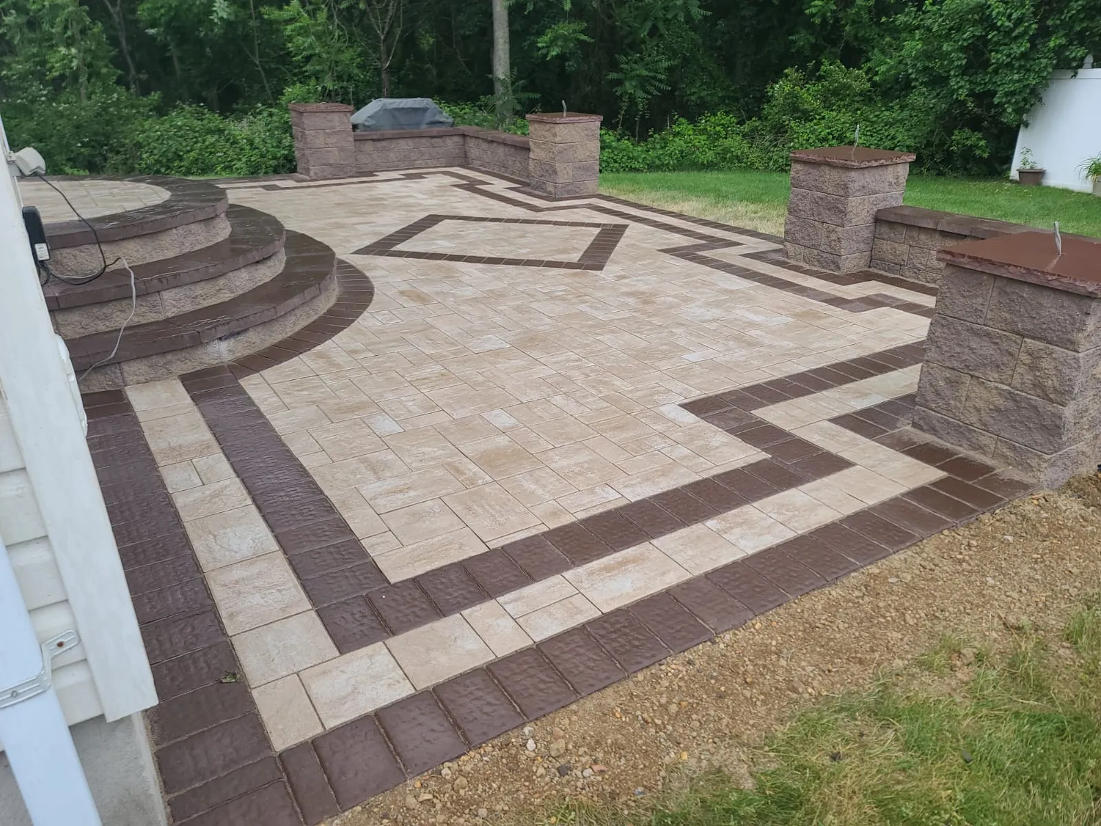 Two-tone paver patio with geometric borders, curved steps, and sitting walls by New Jersey Pavers